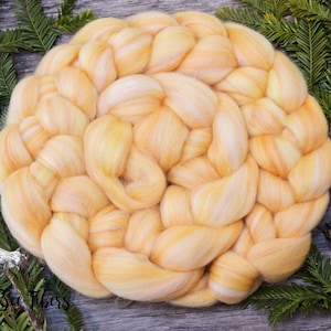 Puede incluir: Un paquete de fibra de alpaca amarilla y blanca trenzada, dispuesto en forma circular. La fibra es suave y esponjosa, y es perfecta para hilar o fieltro.