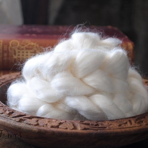 May include: A white, fluffy pile of natural fiber sits in a wooden bowl with intricate carvings. The fiber is arranged in a braided pattern, creating a soft and textured appearance.
