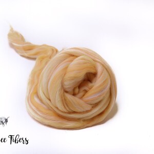 Puede incluir: Primer plano de una bola de vell&oacute;n de lana merino de color naranja claro y blanco. El vell&oacute;n est&aacute; dispuesto en un patr&oacute;n suelto y en espiral.