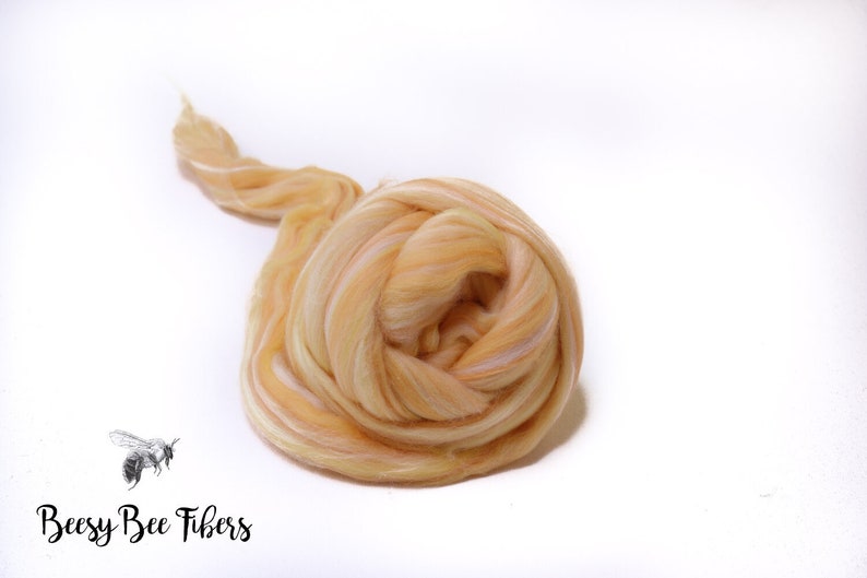 Puede incluir: Primer plano de una bola de vell&oacute;n de lana merino de color naranja claro y blanco. El vell&oacute;n est&aacute; dispuesto en un patr&oacute;n suelto y en espiral.