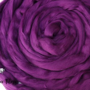 May include: A close-up of a deep purple wool roving, a type of fiber used for spinning yarn or felting. The roving is arranged in a spiral shape, highlighting its soft and fluffy texture.