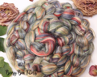 Puede incluir: Una trenza de hilo de colores hilado a mano en tonos de verde, azul, rojo y beige. El hilo está dispuesto en forma circular y tiene un aspecto texturizado. El hilo está etiquetado como "Beesy Bee Fibers".