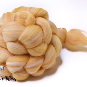 Puede incluir: Una trenza de vell&oacute;n de lana de color naranja claro y blanco. El vell&oacute;n est&aacute; dispuesto en forma de trenza y tiene una cola larga.