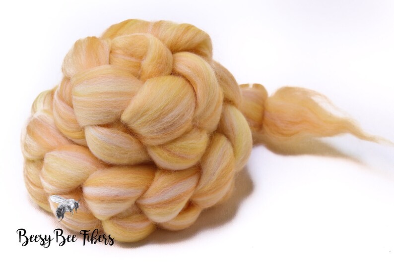 Puede incluir: Una trenza de vell&oacute;n de lana de color naranja claro y blanco. El vell&oacute;n est&aacute; dispuesto en forma de trenza y tiene una cola larga.