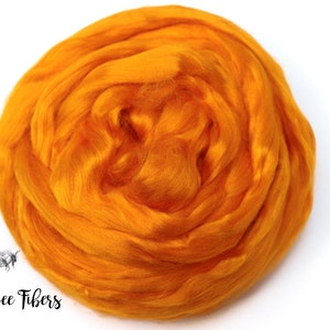 Puede incluir: Primer plano de una bola de fibra de lana de color naranja brillante. La lana es suave y esponjosa, y es perfecta para hilar o fieltro.