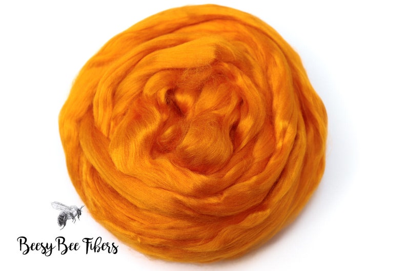 Puede incluir: Primer plano de una bola de fibra de lana de color naranja brillante. La lana es suave y esponjosa, y es perfecta para hilar o fieltro.