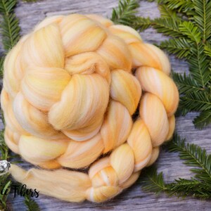 Puede incluir: Un ovillo de lana amarilla y naranja trenzado sobre un fondo blanco. La lana est&aacute; dispuesta en forma circular y est&aacute; rodeada de ramas de pino verdes.