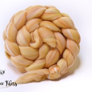 Puede incluir: Una bola trenzada de vell&oacute;n de lana amarilla y naranja con una raya blanca que la atraviesa. El vell&oacute;n est&aacute; hecho por Beesy Bee Fibers.