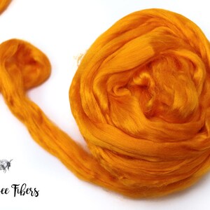 Puede incluir: Primer plano de una fibra de color naranja brillante, probablemente seda o lana, en una bola suelta. La fibra es suave y esponjosa, y es perfecta para hilar o fieltro.
