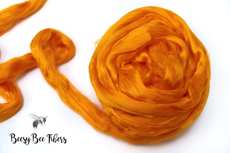 Puede incluir: Primer plano de una fibra de color naranja brillante, probablemente seda o lana, en una bola suelta. La fibra es suave y esponjosa, y es perfecta para hilar o fieltro.