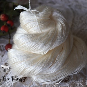 Puede incluir: Un ovillo de hilo de seda blanco, enrollado de forma suelta y listo para tejer o hacer ganchillo. El hilo es suave y delicado, con un brillo sutil.