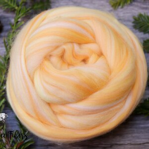 Puede incluir: Primer plano de una bola de vell&oacute;n de lana amarilla y blanca. El vell&oacute;n est&aacute; dispuesto en espiral. El vell&oacute;n est&aacute; sobre una superficie de madera.