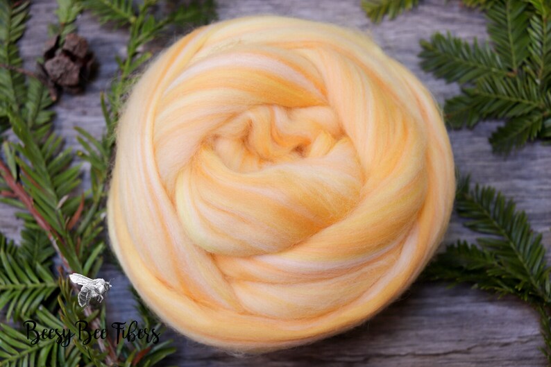 Puede incluir: Primer plano de una bola de vell&oacute;n de lana amarilla y blanca. El vell&oacute;n est&aacute; dispuesto en espiral. El vell&oacute;n est&aacute; sobre una superficie de madera.