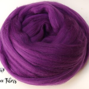 May include: A close-up of a large ball of purple wool roving. The wool is soft and fluffy, and it is perfect for felting or spinning.