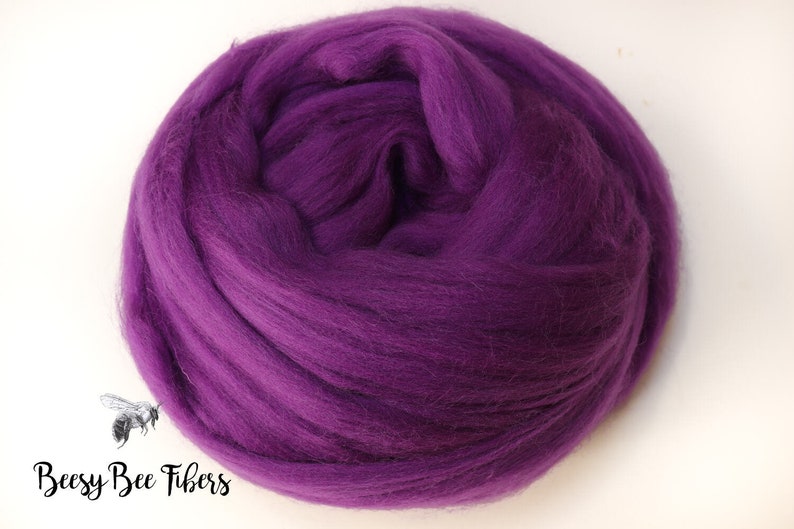 May include: A close-up of a large ball of purple wool roving. The wool is soft and fluffy, and it is perfect for felting or spinning.
