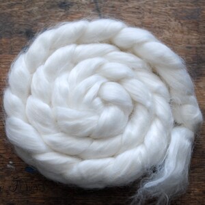 May include: A close-up of a white, fluffy, cotton ball, twisted into a spiral shape. The cotton is soft and appears to be natural.