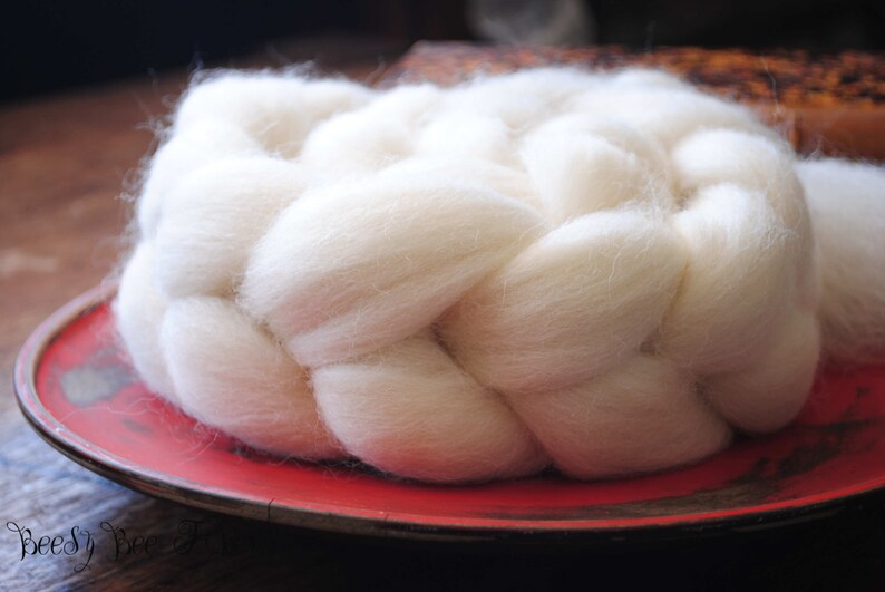 Puede incluir: Primer plano de un hilo blanco, esponjoso y trenzado en un plato rojo. El hilo es suave y parece estar hecho de fibras naturales.