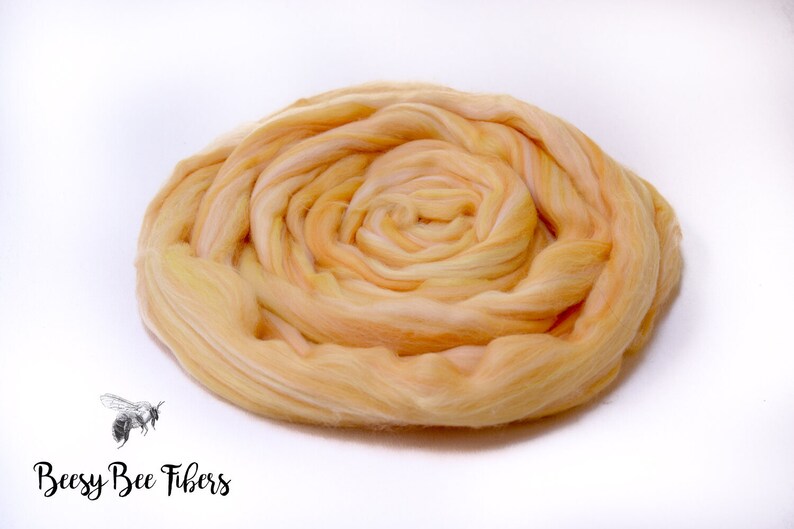 Puede incluir: Primer plano de una fibra suave y esponjosa de color melocot&oacute;n. La fibra est&aacute; dispuesta en espiral, creando una forma circular.