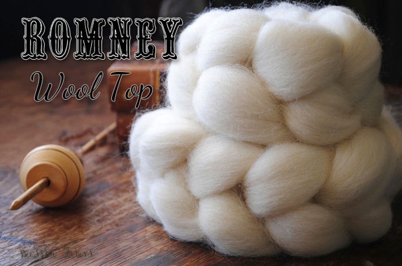 Puede incluir: Primer plano de una lana Romney blanca, un tipo de fibra utilizada para hilar hilo. La lana est&aacute; dispuesta en un patr&oacute;n trenzado, creando una textura suave y esponjosa. La lana est&aacute; sobre una superficie de madera, junto con una rueca de madera.