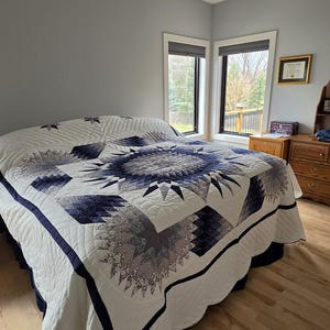 Könnte beinhalten: Eine große, handgefertigte Steppdecke mit einem Sternmuster in Blau-, Grau- und Weißtönen. Die Steppdecke liegt auf einem Bett mit einem weißen Bettrand und einem dunkelblauen Rand. Der Raum hat hellgraue Wände und Holzböden.