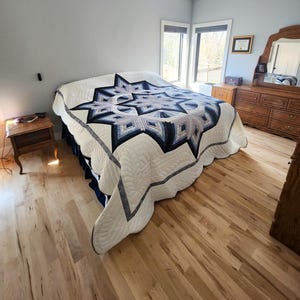 Pode incluir: Uma cama com uma colcha com padrão de estrela em tons de azul, cinza e branco. A colcha é o elemento principal. O quarto tem piso de madeira clara e uma cômoda de madeira. O design da colcha é geométrico.