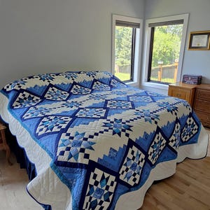 May include: A bed quilt featuring a geometric pattern in shades of navy, royal, and light blue combined with white. The design consists of repeating star motifs and stepped block shapes, finished with a scalloped edge and white backing fabric.