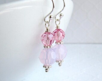 May include: A pair of dangle earrings featuring silver-toned hooks and wire-wrapped connections. Each earring consists of a faceted translucent pink crystal bead positioned above a larger, opaque pale pink bead, finished with small silver-toned accents.