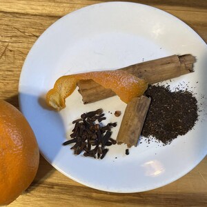 May include: A white plate with orange peel, cinnamon sticks, cloves, and loose leaf tea. The ingredients are for making a spiced tea.
