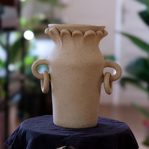 Può includere: Una tazza di ceramica bianca con manico nero e la scritta "But First, Coffee" in grassetto nero. La tazza è posta su uno sfondo sfocato. La tazza è alta circa 10 cm.