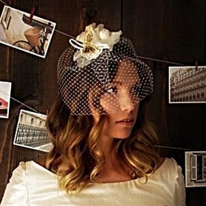 May include: A woman with long brown hair wearing a white veil with a white flower embellishment. The veil is made of a fine mesh material.