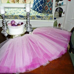 Könnte beinhalten: Ein rosa-weißer Tüll-Tutu-Rock auf einem Holztisch. Der Rock ist aus mehreren Lagen Tüll gefertigt und hat einen Farbverlauf von Weiß zu Rosa.
