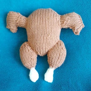 May include: A knitted brown turkey with white feet. The turkey is lying on its back with its wings spread out.