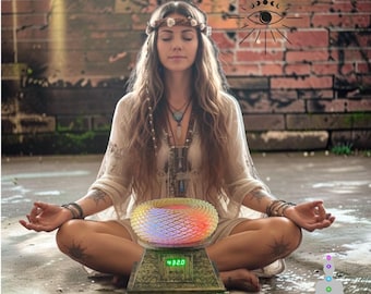 Puede incluir: Una persona en posición de meditación sentada con una túnica clara y una diadema floral. Delante hay un dispositivo con una cúpula brillante, texturizada y multicolor y una pantalla digital que muestra 432.0. El texto dice Natural Sine Wave Energy.