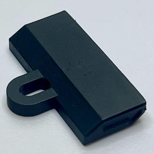 May include: A dark gray plastic hook with a rectangular base and a rounded loop. The hook is designed to be attached to a wall or other surface.