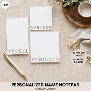 May include: Three white rectangular notepads with personalised names printed in multicoloured letters at the bottom. The names include Tyrell, Emerson, and Brooklyn. A white pen is positioned to the left. Text on the image indicates 40 tear off pages and 16 colour schemes.