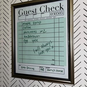 May include: Framed guest check with handwritten order details: maple syrup, coffee, pancakes, hashbrown, and egg yolk. Includes the text "I will always love you x" and "Keep Driving". The frame is metallic.