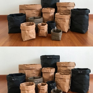 Puede incluir: Un conjunto de 11 bolsas de papel marr&oacute;n y negro de varios tama&ntilde;os. Las bolsas est&aacute;n numeradas del 1 al 11.
