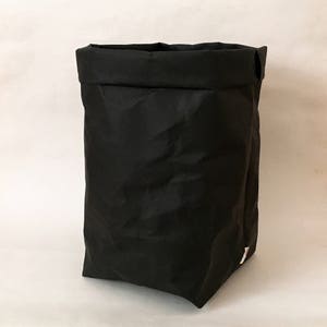 Puede incluir: Un contenedor de almacenamiento de tela negro con una parte superior doblada. El contenedor est&aacute; hecho de un material suave y arrugado.