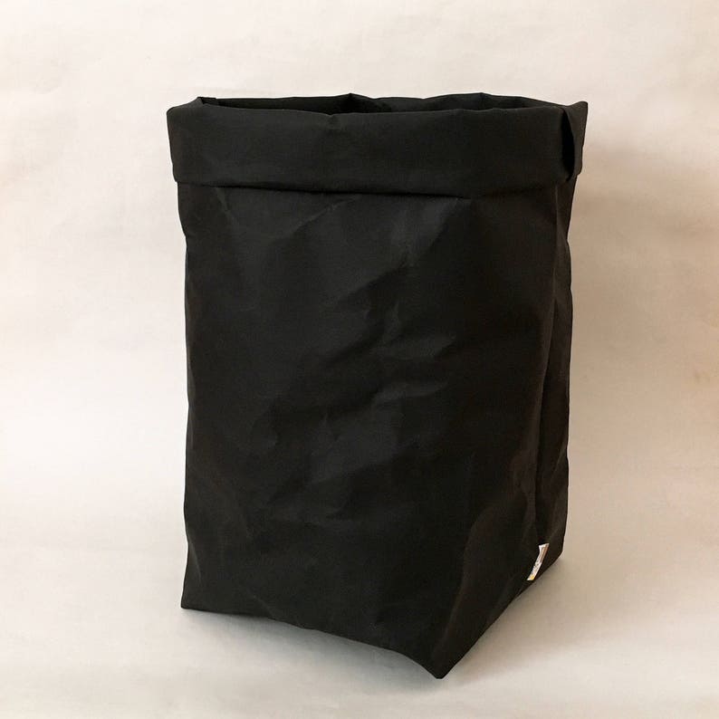 Puede incluir: Un contenedor de almacenamiento de tela negro con una parte superior doblada. El contenedor est&aacute; hecho de un material suave y arrugado.