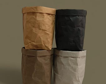 May include: Four paper storage bags in shades of brown, black, and gray are stacked. The bags have a crumpled texture and a folded-over top edge. The bags are likely for home organization or decor.