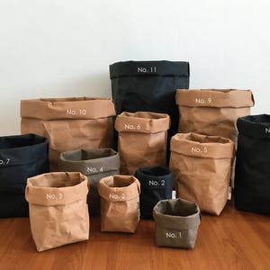 Puede incluir: Once bolsas de papel marr&oacute;n de varios tama&ntilde;os con n&uacute;meros blancos en ellas. Las bolsas est&aacute;n dispuestas en una fila sobre una superficie de madera. Las bolsas est&aacute;n todas hechas de papel marr&oacute;n natural y tienen una textura arrugada. Los n&uacute;meros en las bolsas van del 1 al 11.