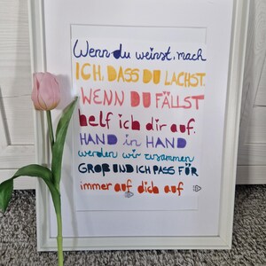Può includere: Una stampa incorniciata con testo manoscritto colorato in tedesco, tra cui le frasi "Wenn du weinst, mach" e "immer auf dich auf." Un tulipano rosa con foglie verdi è posizionato a sinistra della cornice. La cornice è bianca.