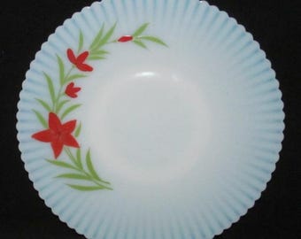 May include: A white, scalloped-edge dish with a light blue rim and floral design. The dish features red flowers and green leaves. The rim has a ribbed texture. The background is black.