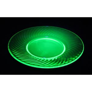 May include: A green glass plate with a swirl design. The plate is glowing under a black light.