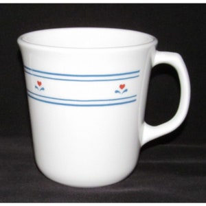 May include: White ceramic mug with a blue band design and small red heart accents. The mug has a curved handle and a simple, classic shape. A perfect addition to any kitchen or coffee collection.