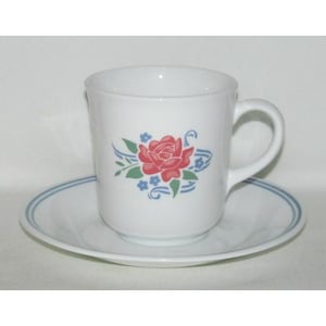 May include: White ceramic mug and saucer set. The mug features a red rose design with blue and green accents. The saucer has a blue trim. A classic floral design for everyday use.