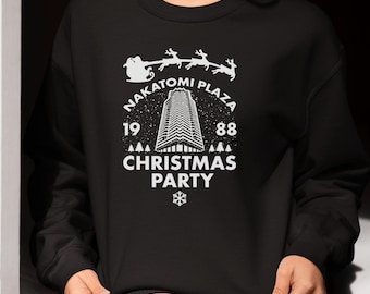 May include: Black sweatshirt with a white graphic featuring the text "Nakatomi Plaza Christmas Party 1988". The design includes a skyscraper, Santa's sleigh with reindeer, Christmas trees, and a snowflake.