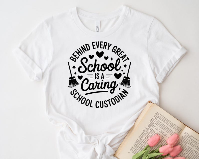 May include: White t-shirt with a black graphic that reads "Behind Every Great School Is a Caring School Custodian." The design includes hearts, stars, and brooms. A book and pink flowers are in the bottom right corner.
