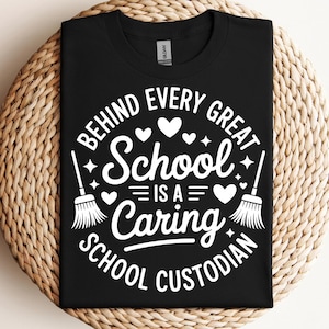 以下が含まれることがあります： 「BEHIND EVERY GREAT SCHOOL IS A CARING SCHOOL CUSTODIAN」と書かれた白いグラフィックが特徴の黒いTシャツ。デザインにはハート、星、ほうきのイラストが含まれています。シャツは織られた円形の表面に表示されています。