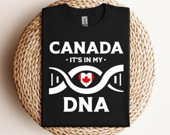 Pode incluir: Camiseta preta com texto branco que diz "CANADA - IT'S IN MY DNA". Abaixo do texto, há uma cadeia de ADN branca com um coração de bandeira canadiana vermelha e branca no centro.
